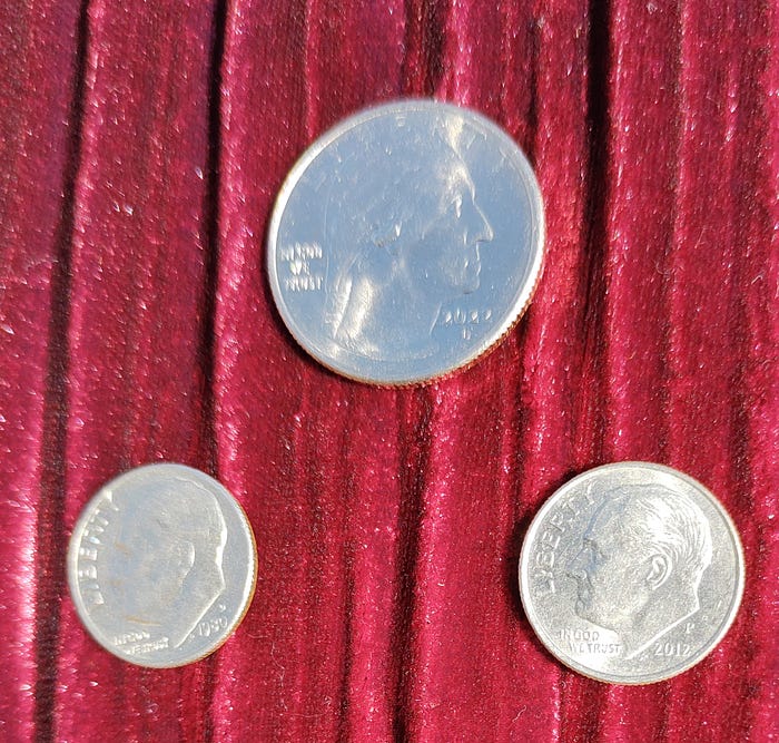 3 silver coins, heads side facing up, a quarter and 2 dimes totaling forty-five cents are in a pyramid formation laid on burgundy velvet fabric